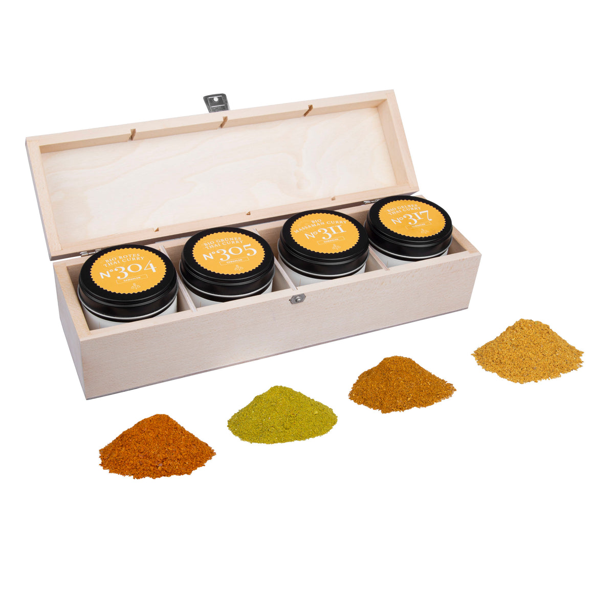 Holzbox mit vier Gewürzgläsern, beschriftete Deckel, davor Bio Thai Curry Gewürze als Pulver.
