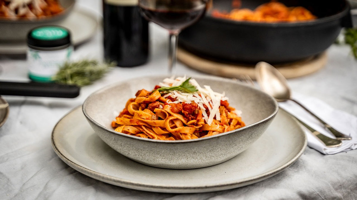 Tagliatelle mit Tomatensauce und Käse, dazu ein Glas Wein im Hintergrund.