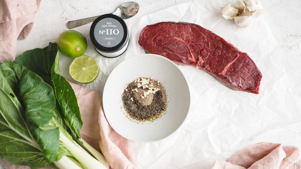 Rohes Steak, Bok Choy, Limette, Knoblauch und grober schwarzer Pfeffer in einer Schüssel auf Weiß.