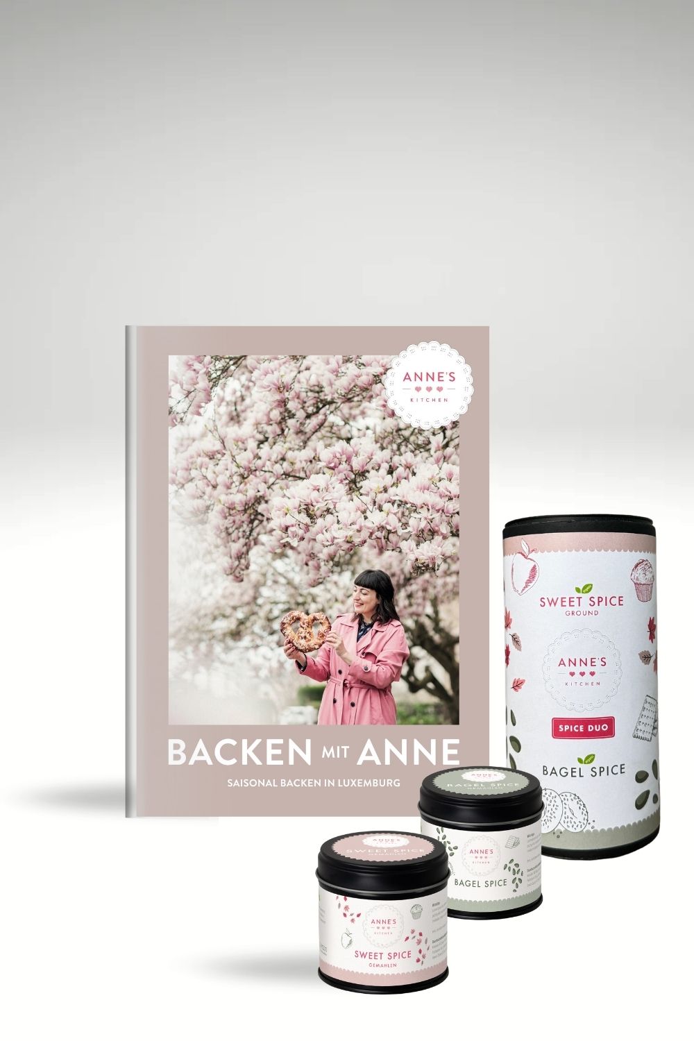 Geschenkset mit Backbuch, drei blumigen Gewürzgläsern und Bagel-Gewürz, Frau unter blühendem Baum.