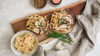 Zwei Waffeln mit gegrilltem Hähnchen und Krautsalat auf einem Holzbrett, bestreut mit Gewürzen.