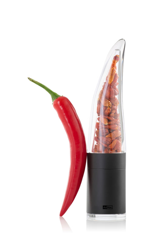 Rote Chilischote neben Chilischneider Pepe schwarz, gefüllt mit getrockneten Chilischoten.