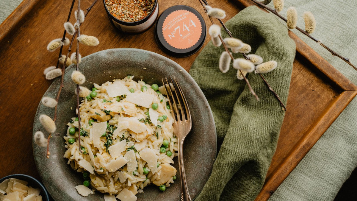 Eine Schüssel Pasta mit Erbsen, Käse und Gewürzen, daneben eine Gabel, eine grüne Serviette und Weidenzweige.