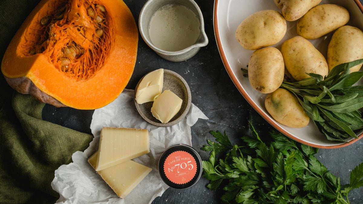 Kürbis, Kartoffeln, Käse und frische Kräuter mit Butter und Sahne vor dunklem Hintergrund.