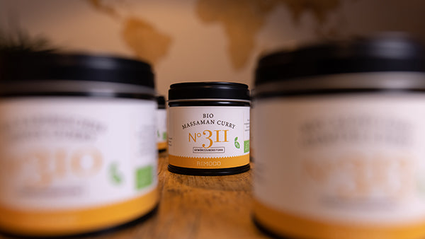 Bio Curry Gewürz-Set N°1 Glas im Fokus, umgeben von unscharfen Gläsern auf einem Holztisch.