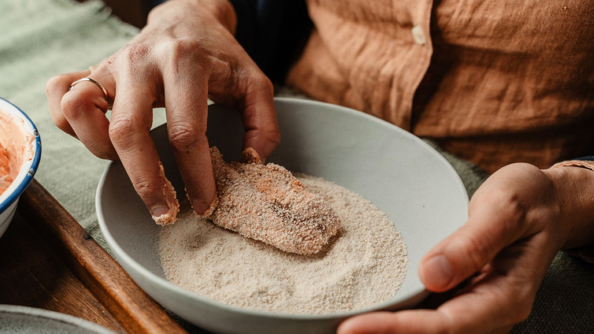 Eine Person paniert ein Schnitzel von Hand mit Semmelbröseln.