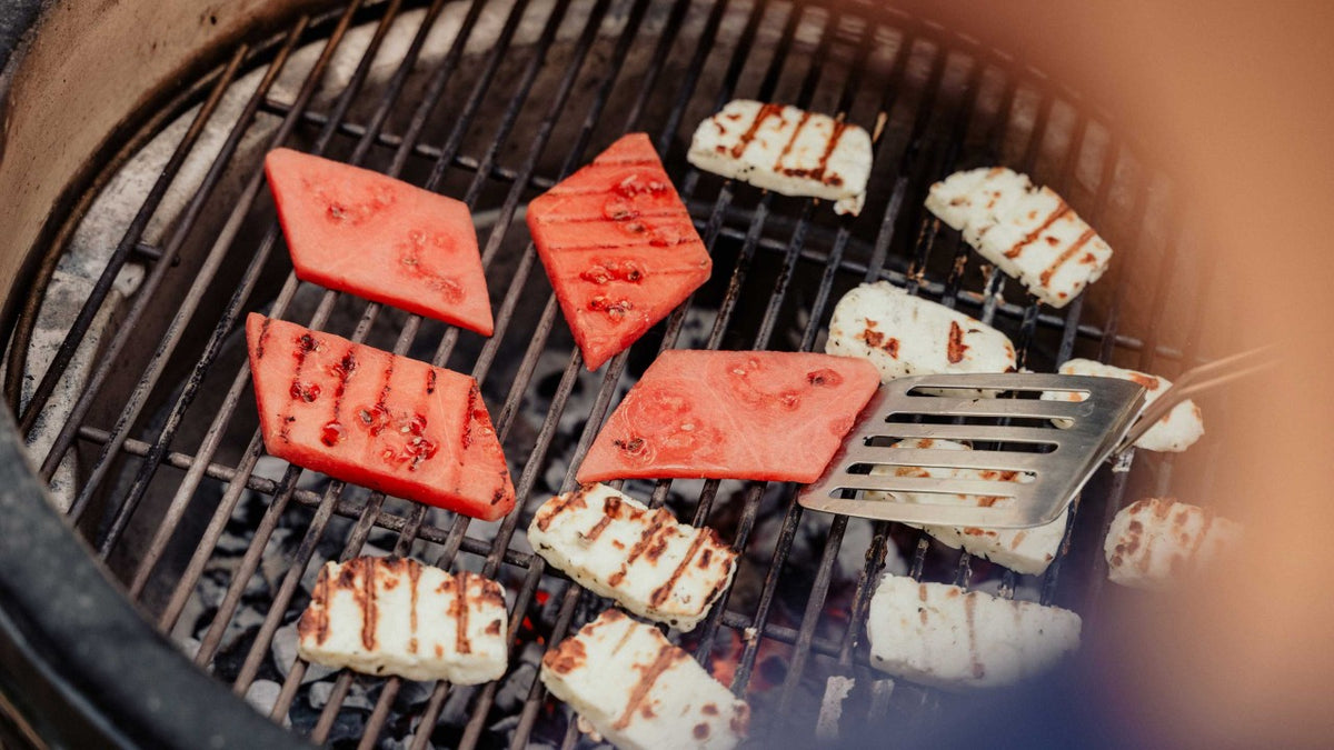 Gegrillter Halloumi und Wassermelonenscheiben auf dem Grill, daneben ein bereitliegender Spatel.