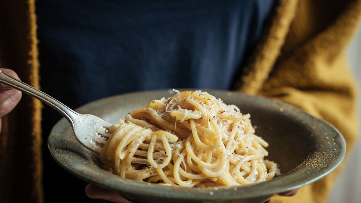 Spaghetti mit geriebenem Käse und grobem schwarzem Pfeffer werden in einer Schüssel vermengt.