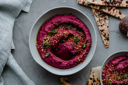 Schale mit rotem Rote-Bete-Hummus, bestreut mit Kräutern und Samen, dazu Fladenbrot.