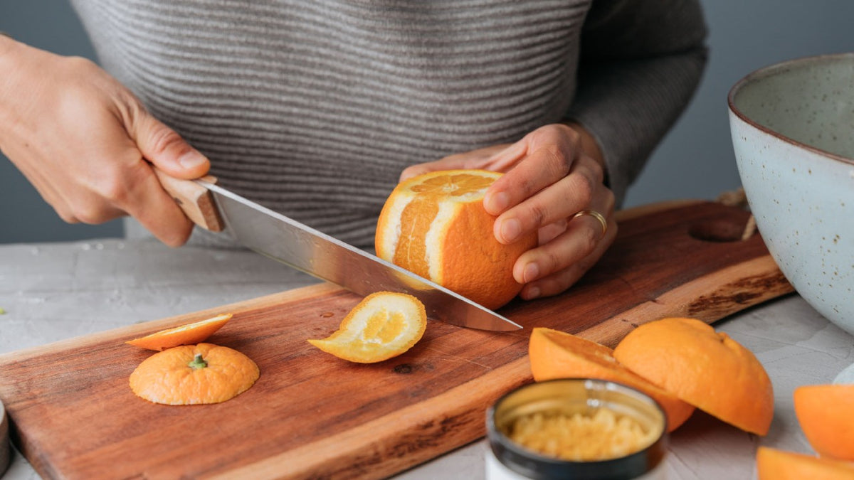 Eine Person schält eine frische Orange mit einem Messer auf einem Holzschneidebrett.