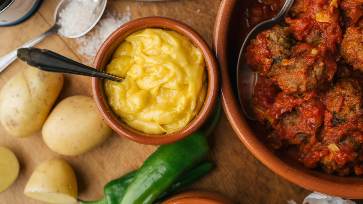 Fleischbällchen in Tomatensauce, gelber Sauce, Kartoffeln und grüner Paprika auf einem Holztisch.