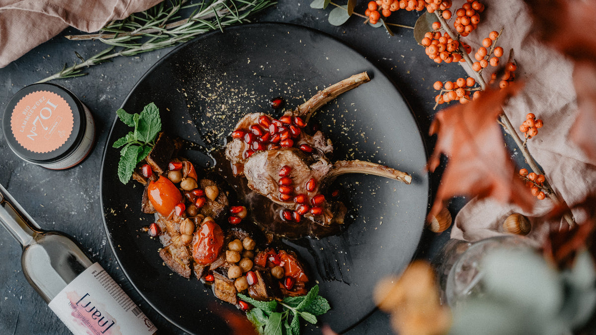 Lammkoteletts mit Kichererbsen, Tomaten und Granatapfelkernen auf schwarzem Teller.