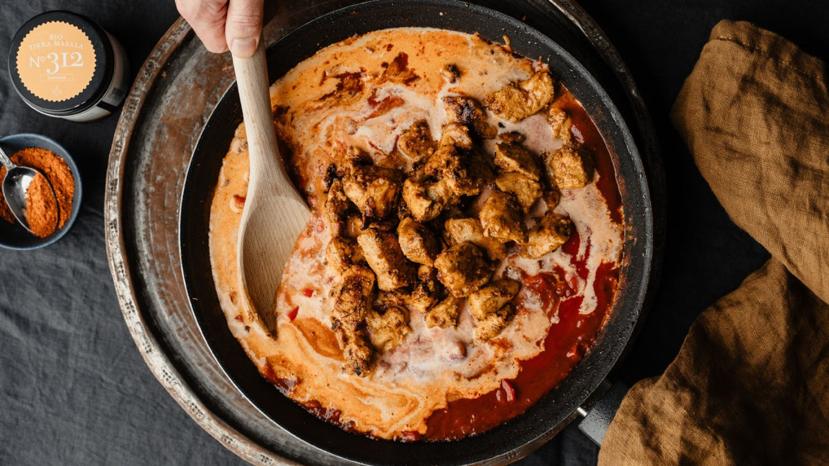 Hähnchenstücke garen in cremiger Currysauce, während eine Hand mit einem Holzlöffel umrührt.