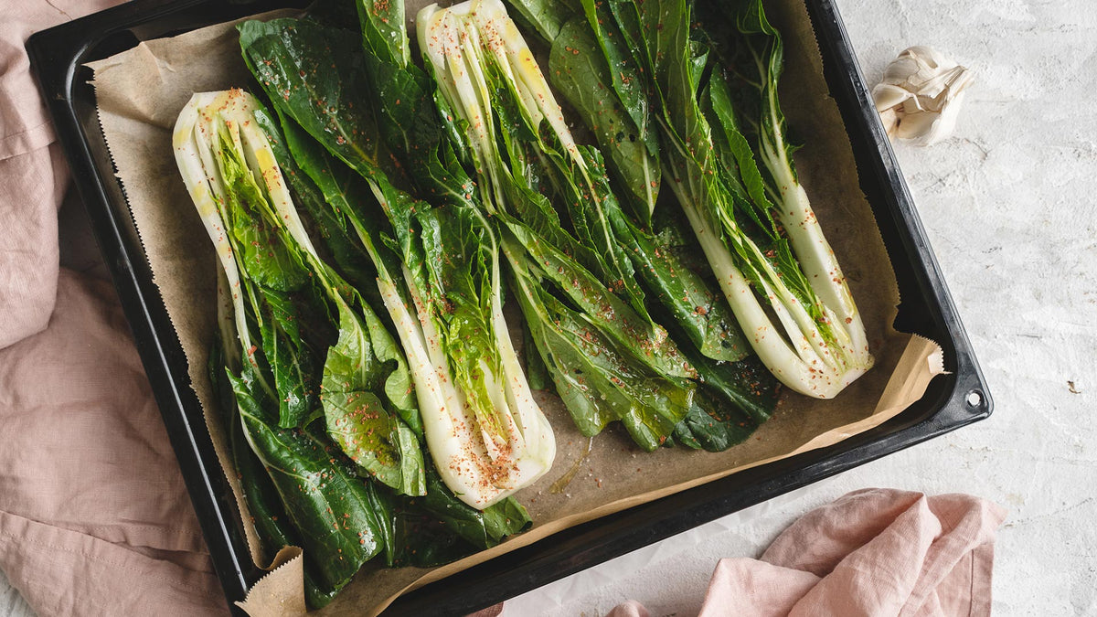 Gewürzte Pak-Choi-Hälften auf einem Backblech, bereit zum Rösten.