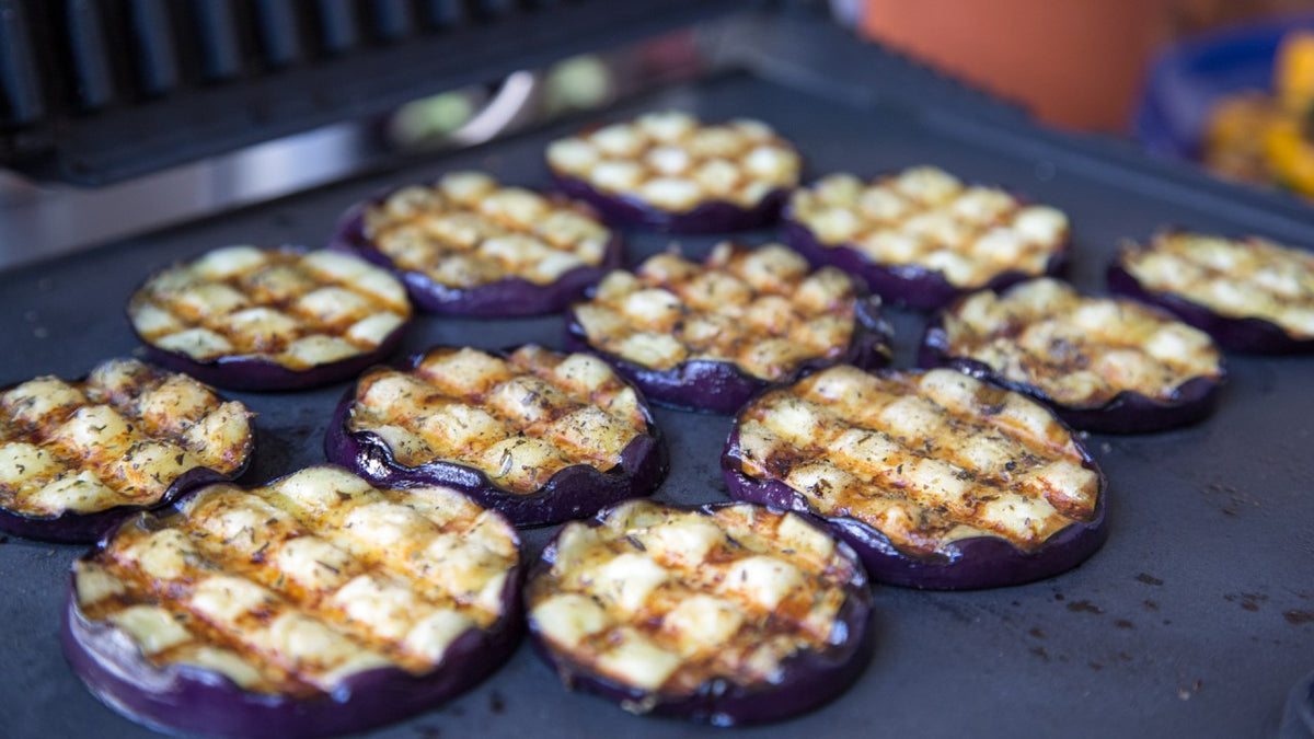 Gegrillte Auberginenscheiben mit sichtbaren Kräutern und Gewürzen auf einer Grillplatte.
