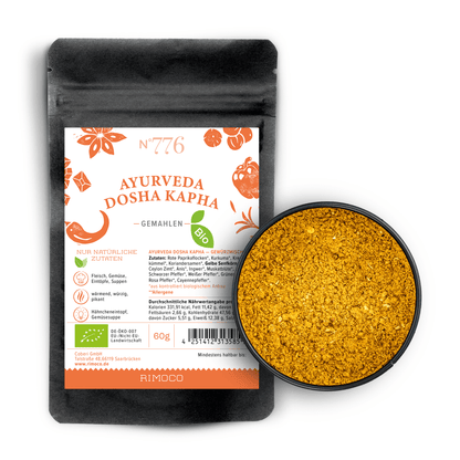 Schwarzer Beutel mit Aufschrift Bio Ayurveda Dosha Kapha neben einer Schale gelbes Bio-Gewürzpulver.