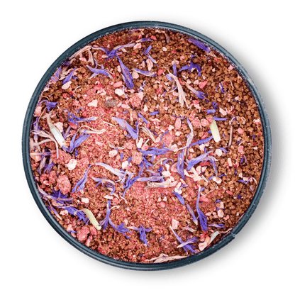 Bio Ayurveda Früchtetraum: Runddose mit rosa Fruchtpulver, darauf lila Blütenblätter.