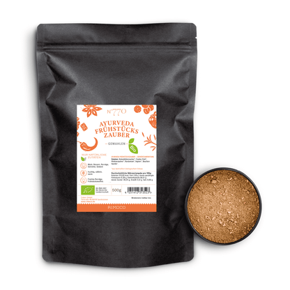 Bio Ayurveda Frühstückszauber in schwarzer Tüte mit braunem Pulver sichtbar daneben.