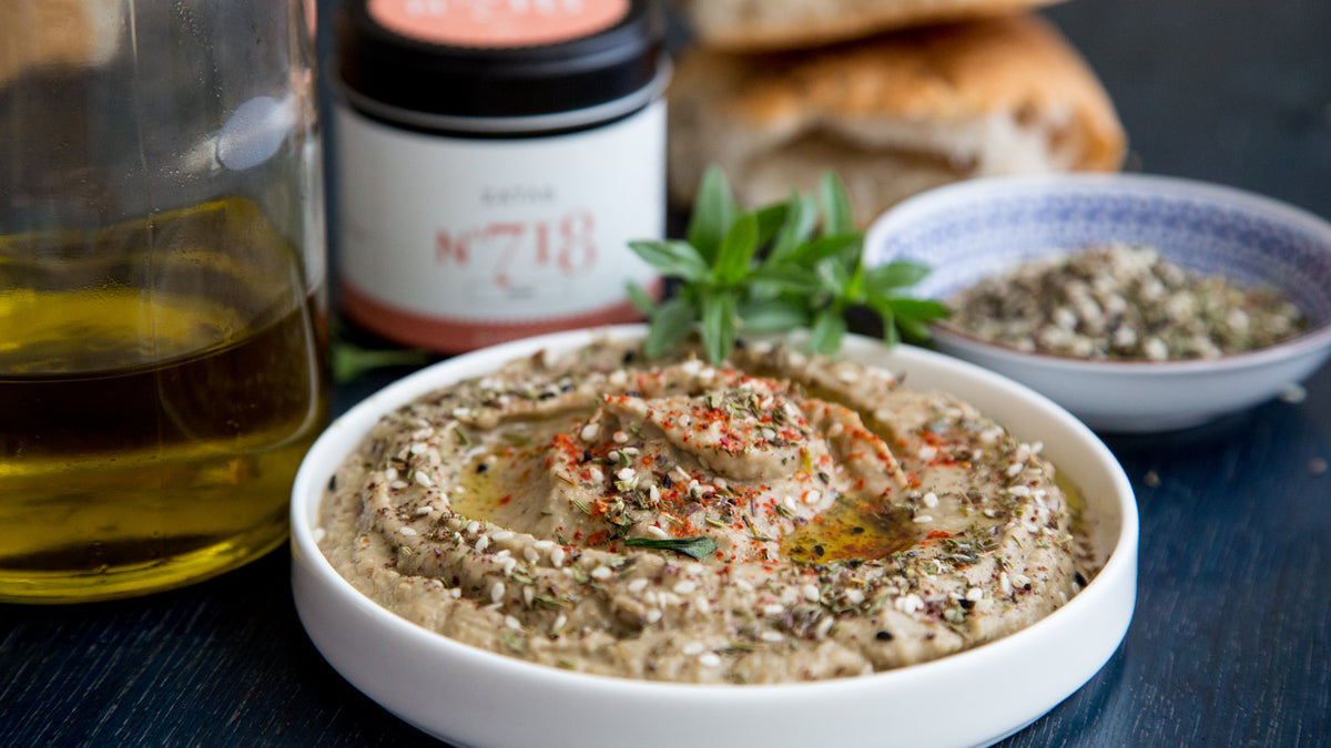 Eine Schale Dip mit Kräutern und Öl, dahinter Gewürzset Ottolenghi Simple und Brot.
