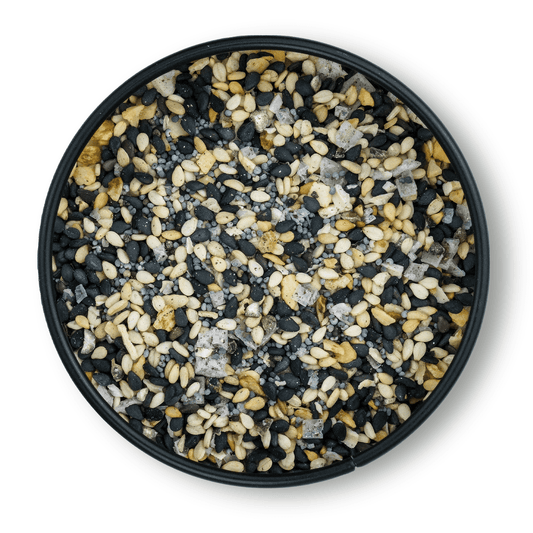 Schwarze Schale mit Bio Bagel Gewürz, schwarze und weiße Sesamsamen, grobes Salz, Draufsicht.