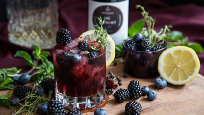 Zwei Beerencocktails mit Zitrone und Kräutern neben Geschenkset mit Gin und würzigen Botanicals.