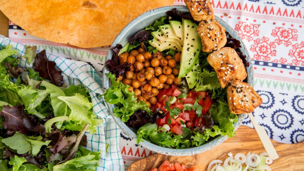 Salatschüssel mit Blattsalat, Kichererbsen, Avocado, Tomaten und gegrillten Tofuspießen.