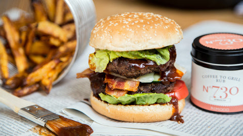 Ein gestapelter Cheeseburger mit Pommes steht neben einer Glas Grillgewürze Geschenkbox N°2.