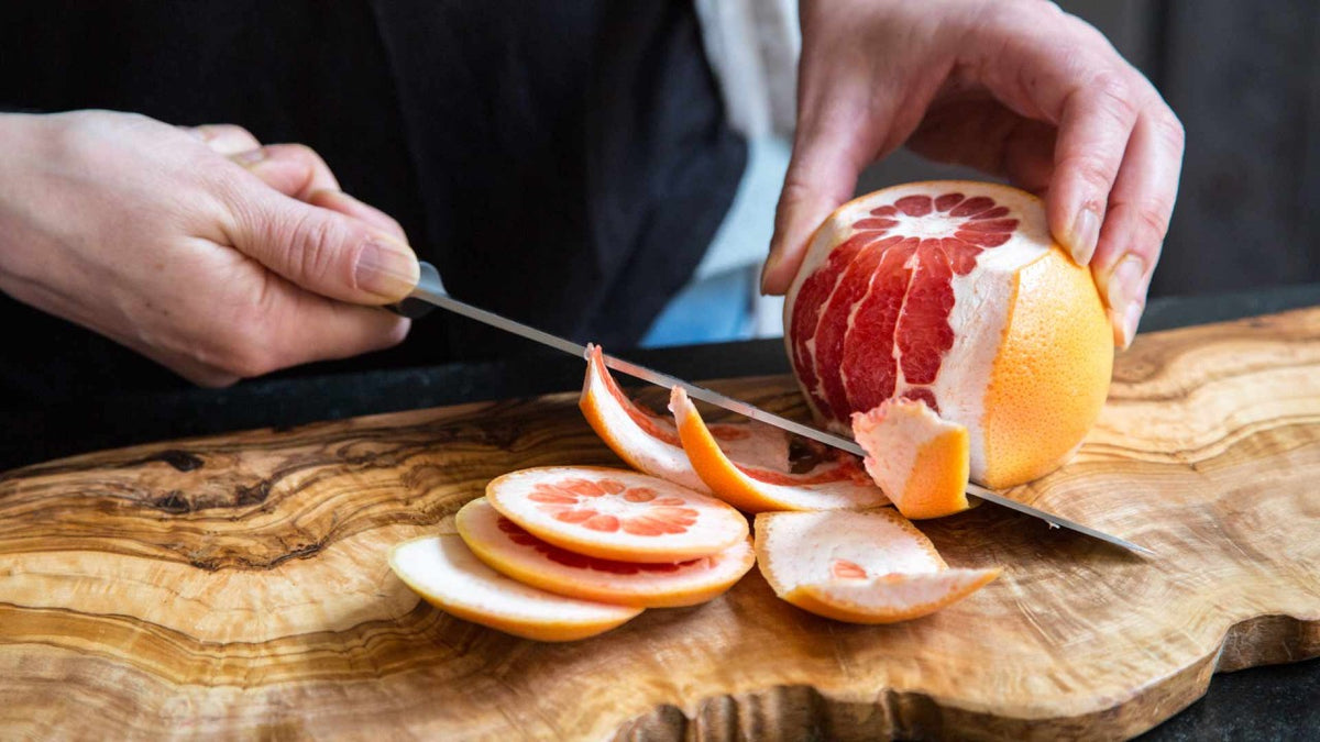 Eine Person schält eine frische Grapefruit mit einem Messer auf einem Holzbrett.