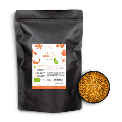 Bio Cajun Gewürz in schwarzer Tüte, daneben eine Schale mit orange-gelb gemahlenem Gewürz.