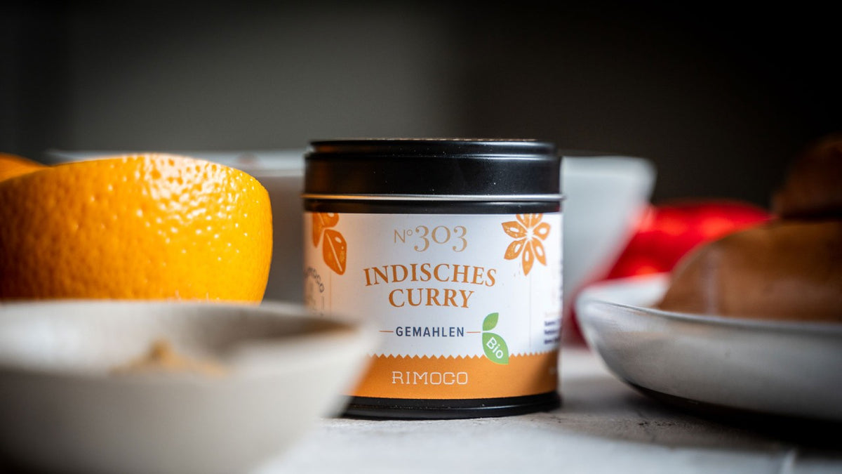 Eine Dose mit der Aufschrift „Indisches Curry“ steht neben Orangenscheiben und Schüsseln auf der Arbeitsplatte.