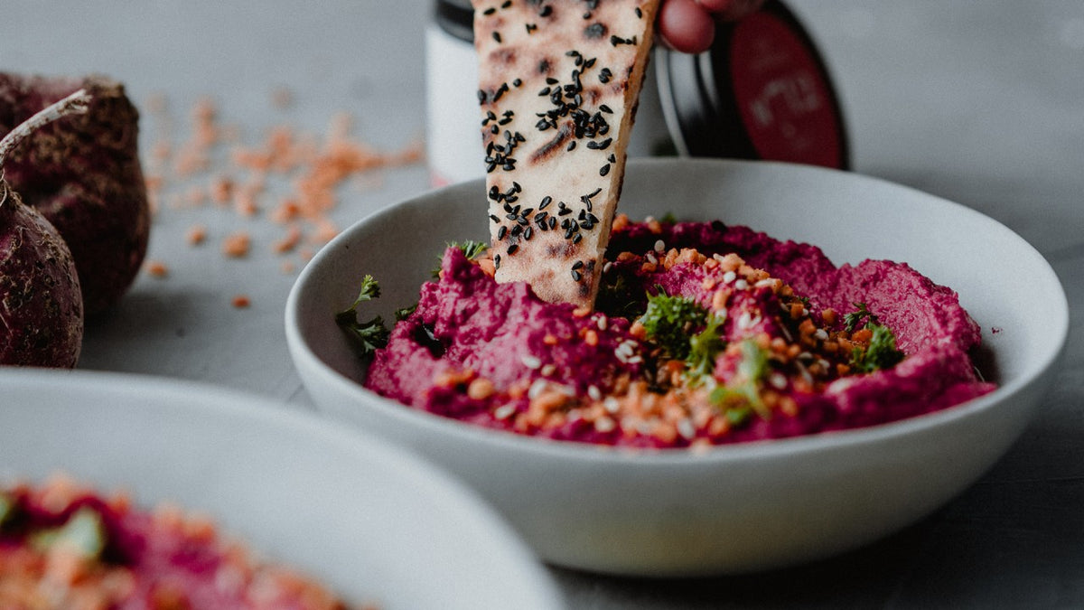 Rote-Bete-Hummus mit frischen Kräutern und Samen, dazu Fladenbrot zum Dippen.