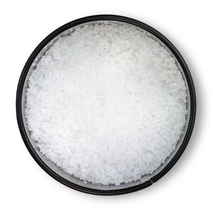 Runde schwarze Schale mit grobem Fleur de Sel de Camargue von oben auf weißem Hintergrund.
