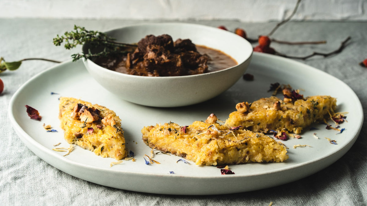Eine Schüssel Eintopf mit drei Scheiben Maisbrot, garniert mit frischen Kräutern und Nüssen.