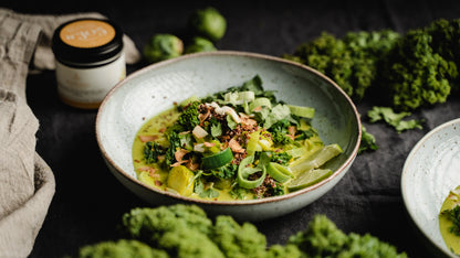 Schüssel mit Salat aus Avocado, Grünkohl, Quinoa und Lauch neben einer Thai Curry Geschenkbox.