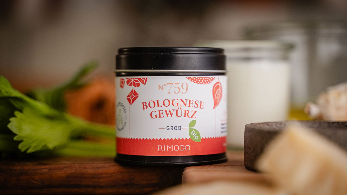Auf einem Tisch steht ein Glas Bolognese-Gewürz, im Hintergrund liegen Gemüse und Käse.