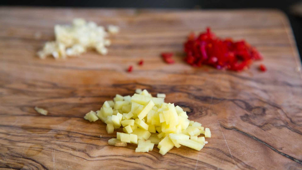 Gehackter Ingwer, Knoblauch und rote Chilischoten liegen auf einem Holzschneidebrett.