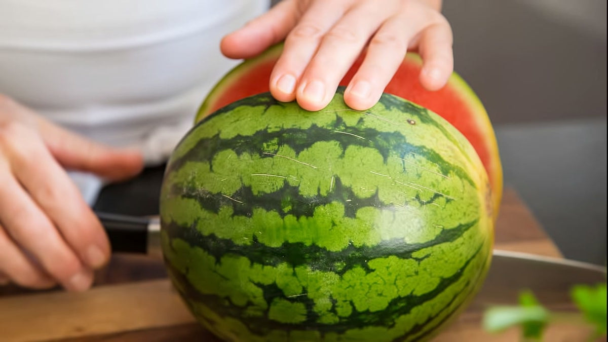 Eine Person schneidet eine Wassermelone mit einem Messer auf einem Holzbrett auf.