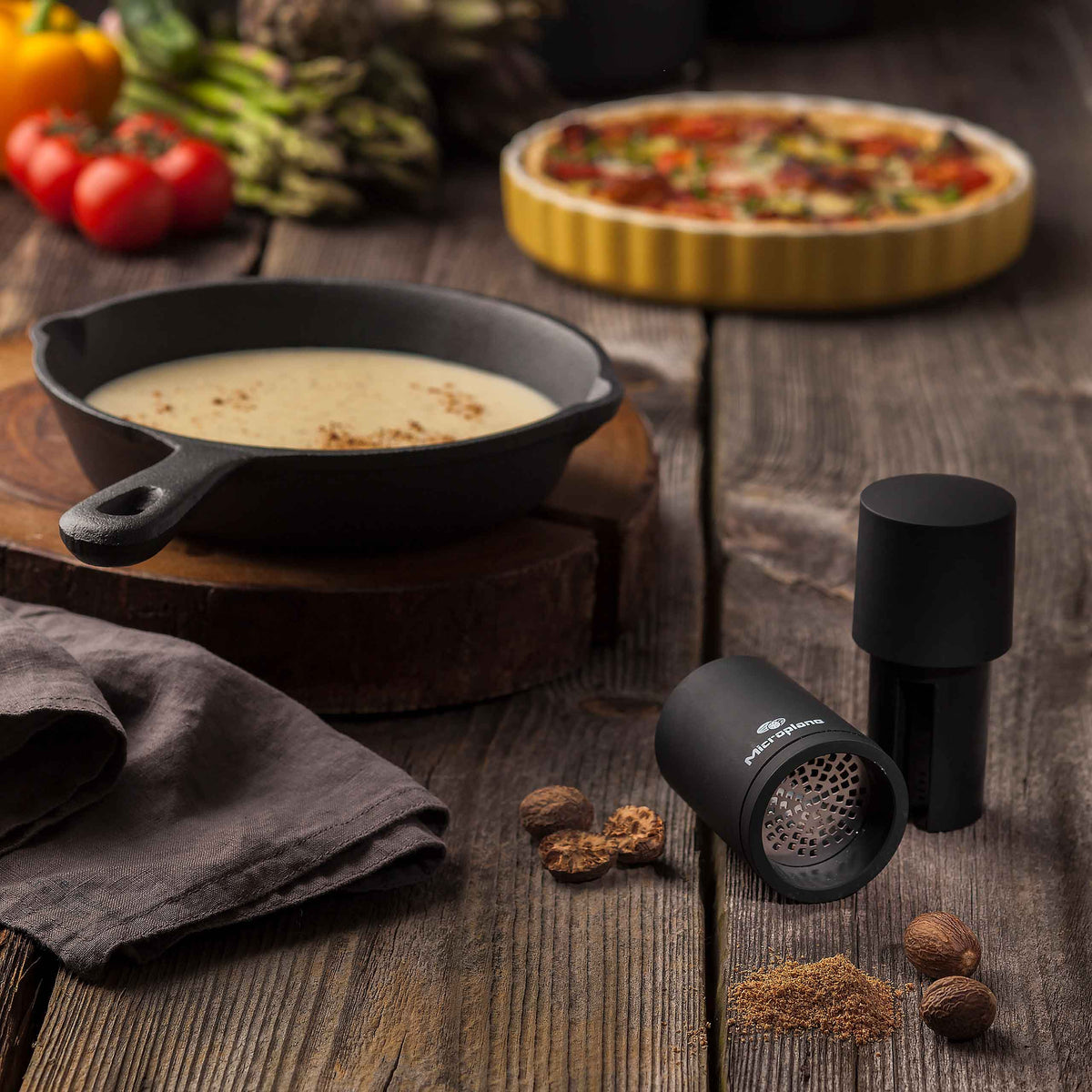 Eine Pfanne Suppe, eine Microplane Muskatmühle 2 in 1 und ganze Muskatnüsse auf Holztisch.