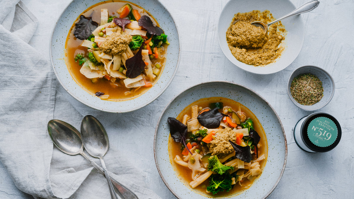 Zwei Schalen Gemüsesuppe mit Blattgemüse, daneben ein magnetisches Gewürzregal mit 12 Gewürzen.