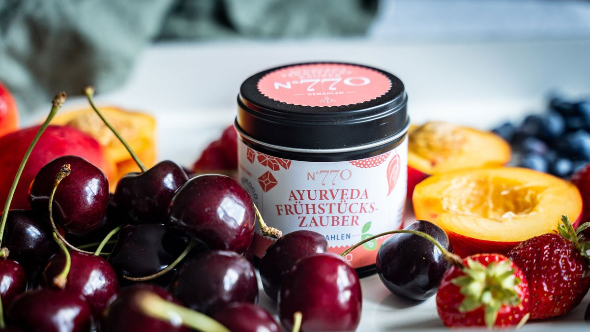 Ayurveda-Frühstückszauber im Glas, umgeben von Kirschen, Pfirsichen und Erdbeeren.