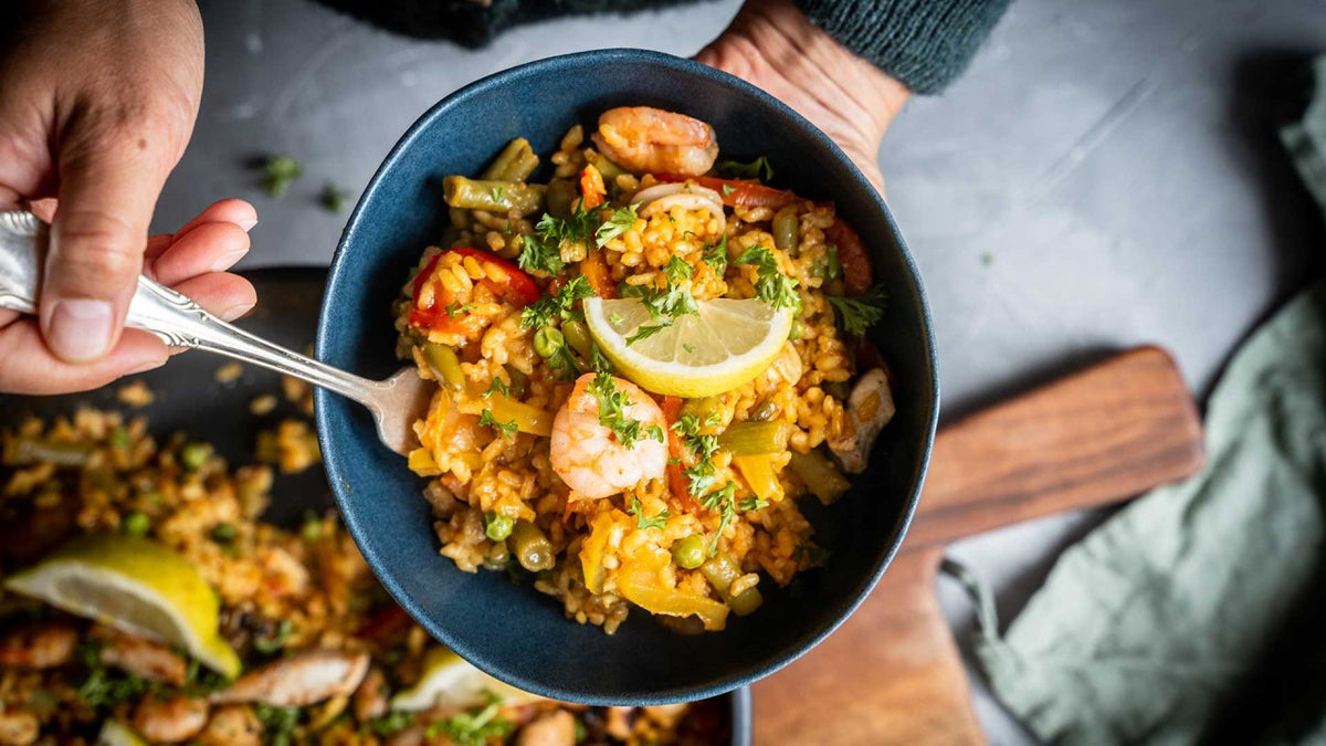 Eine Schüssel spanische Meeresfrüchte-Paella mit Garnelen, Erbsen und Reis, die von einer Person gehalten wird.