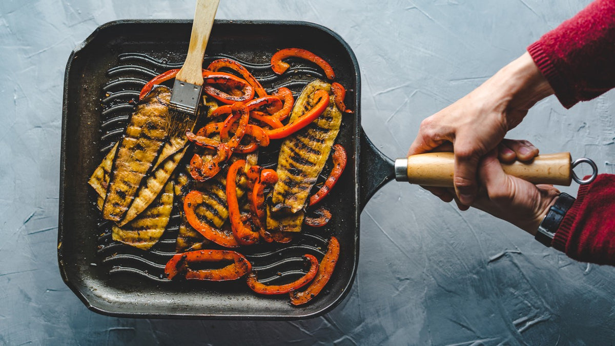 Auberginenscheiben und rote Paprika werden in einer Pfanne gegrillt und mit Marinade bestrichen.