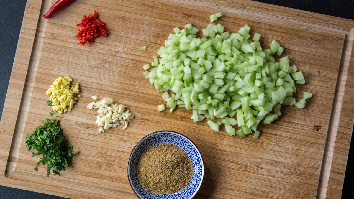 Gehackte Gurke, Chili, Ingwer, Knoblauch, Kräuter und gemahlene Gewürze auf einem Schneidebrett.