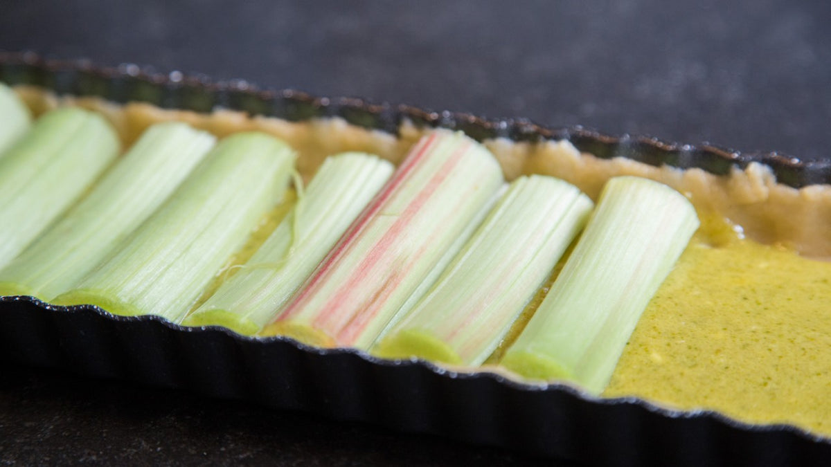 Rohkost-Rhabarber-Tarte mit frischen Stangen auf gelber Füllung in einer Tarteform.