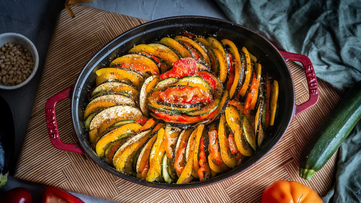 Bunte Gemüsescheiben, spiralförmig in einer roten Auflaufform angeordnet.