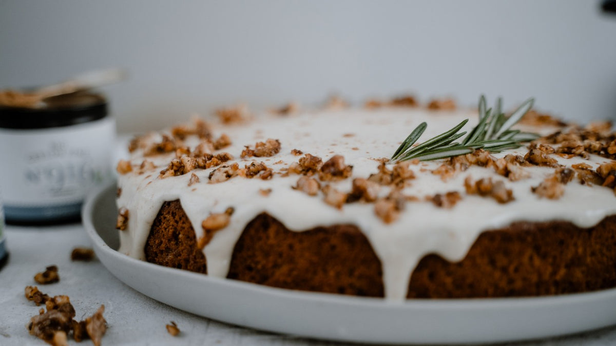 Karottenkuchen mit weißer Glasur, gehackten Walnüssen und etwas Rosmarin auf einem rustikalen Teller.