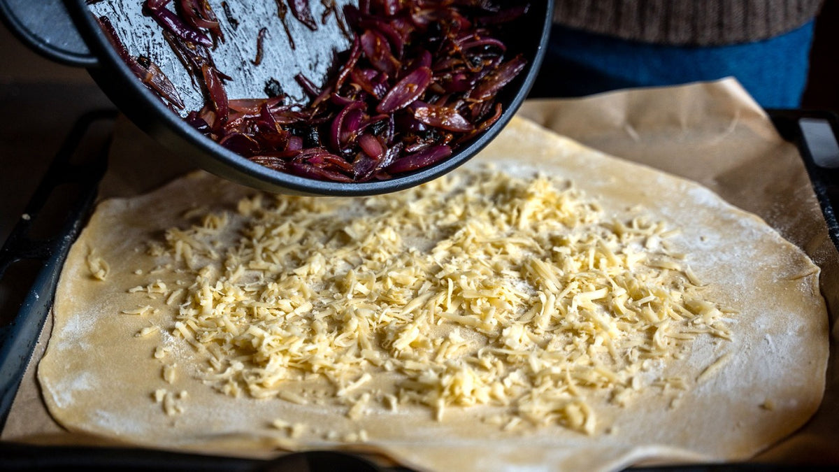 Die gedünsteten Zwiebeln werden auf geriebenem Käse und Teig auf Backpapier verteilt und sind nun bereit zum Backen.