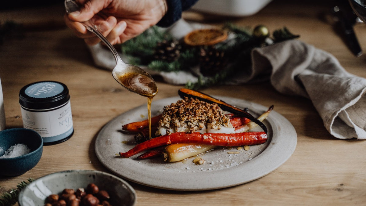 Geröstete Karotten und zarter Fisch, darüber träufelt ein Löffel eine helle Sauce.
