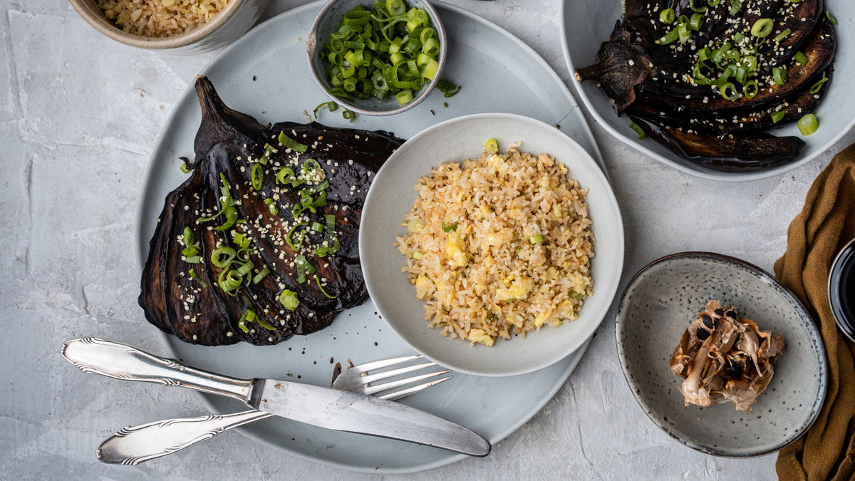 Gebratene Aubergine, gebratener Reis und Bio Schwarzer Knoblauch auf grauen Keramiktellern.