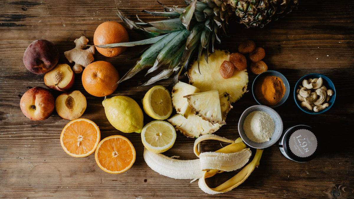 Geschnittene Ananas, Zitrusfrüchte, Banane, Nüsse und Gewürze, auf einem rustikalen Holztisch angerichtet.